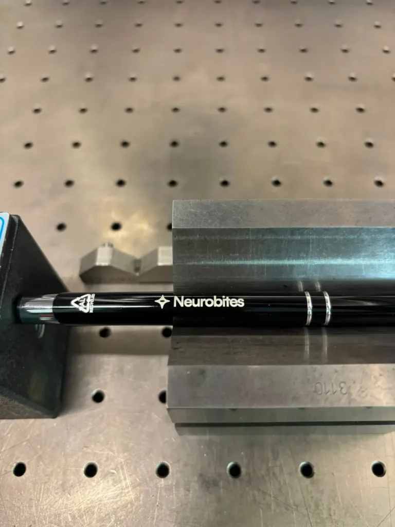Schwarzer Kugelschreiber mit Lasergravur des Neurobites-Logos auf dem Gravurtisch